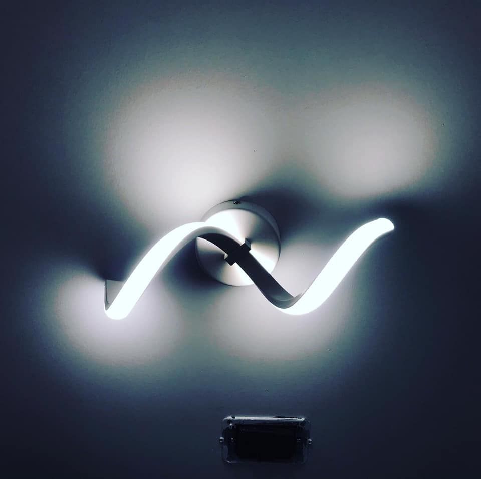 Applique da parete a LED moderna e vorticosa, che crea una luce brillante su una parete scura.