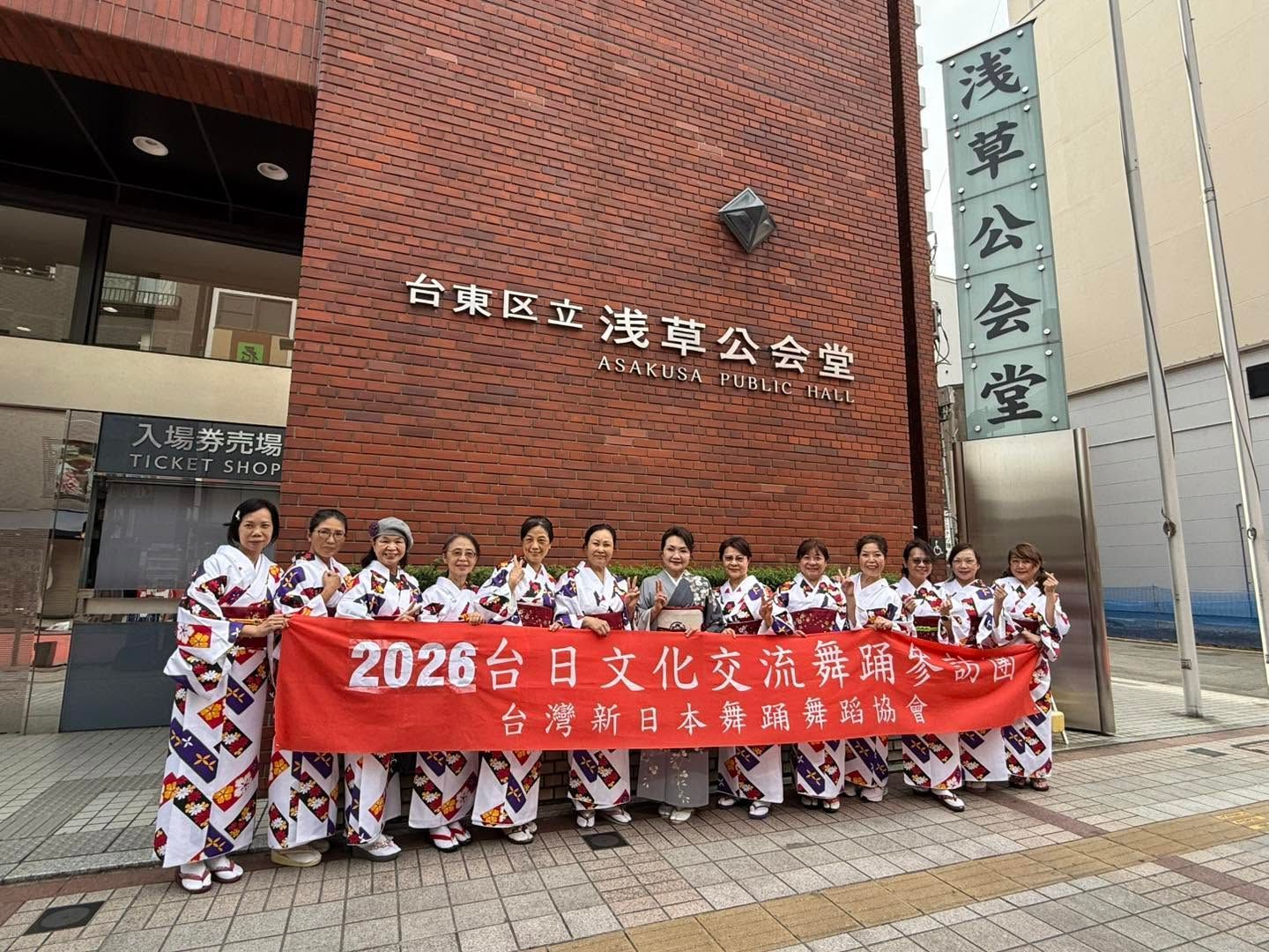 People holding a red banner in front of a brick building with Chinese signage and a vertical plaque.