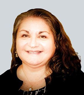 A woman with long hair is smiling and wearing a black jacket and a necklace. A woman with long hair is smiling and wearing a black jacket and a necklace.