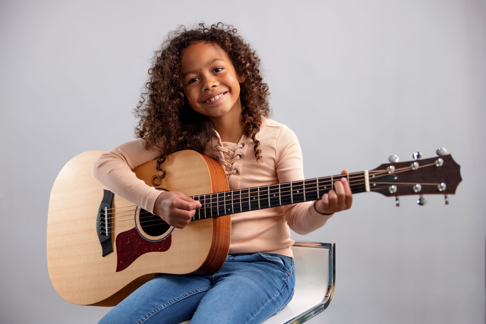 A young girl is sitting on a stool playing an acoustic guitar. A young girl is sitting on a stool playing an acoustic guitar.