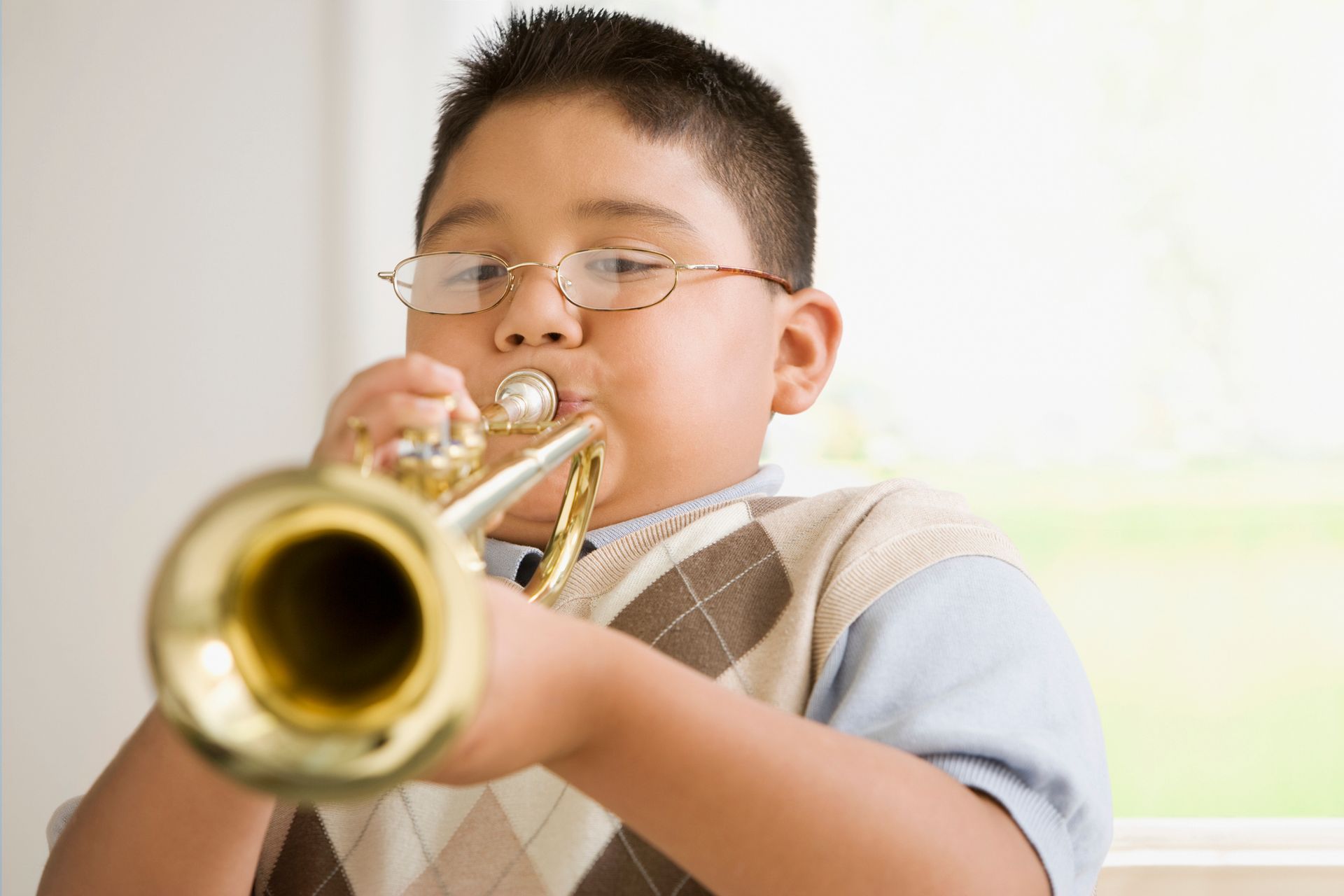 A young boy wearing glasses is playing a trumpet. A young boy wearing glasses is playing a trumpet.
