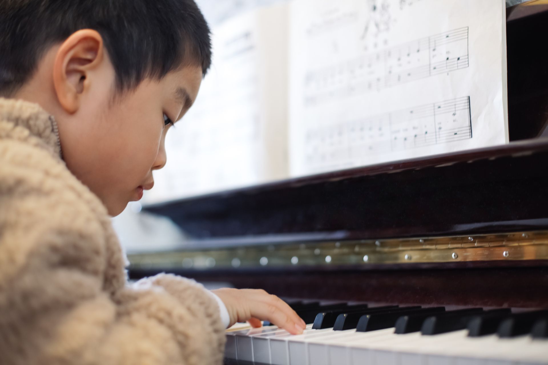 A young boy is playing a piano with sheet music in the background. A young boy is playing a piano with sheet music in the background.