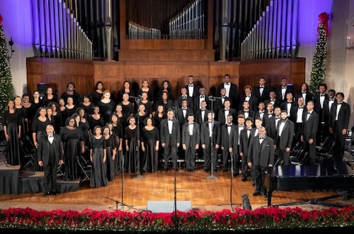 Choir performing on stage in formal attire; Christmas decorations and pipe organ in the background. Choir performing on stage in formal attire; Christmas decorations and pipe organ in the background.