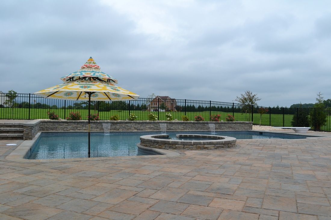 Pool with blue water and concrete edging, surrounded by a green lawn and fence.