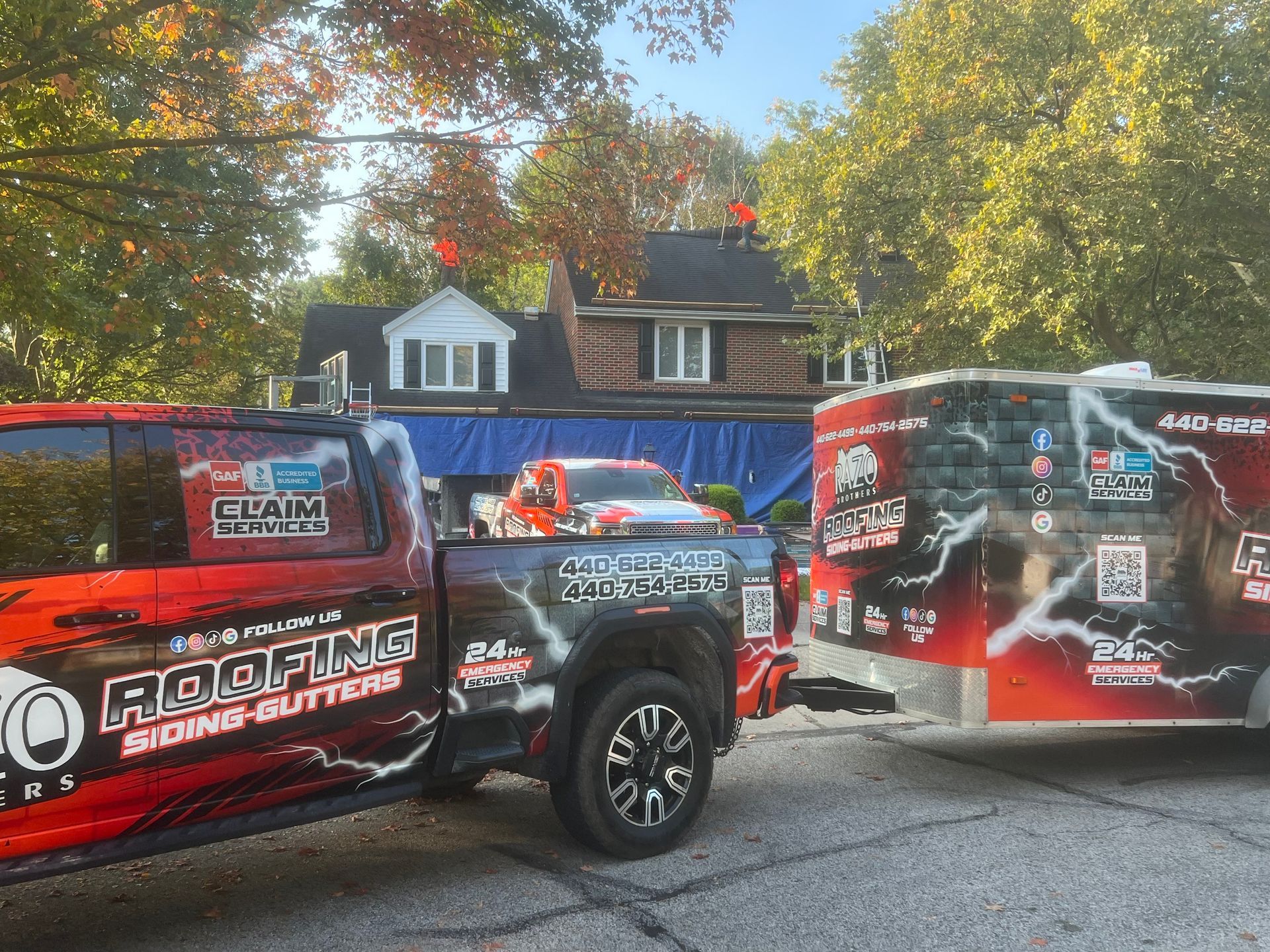 Truck and trailer with roofing company logo parked in front of a house undergoing roof repair.