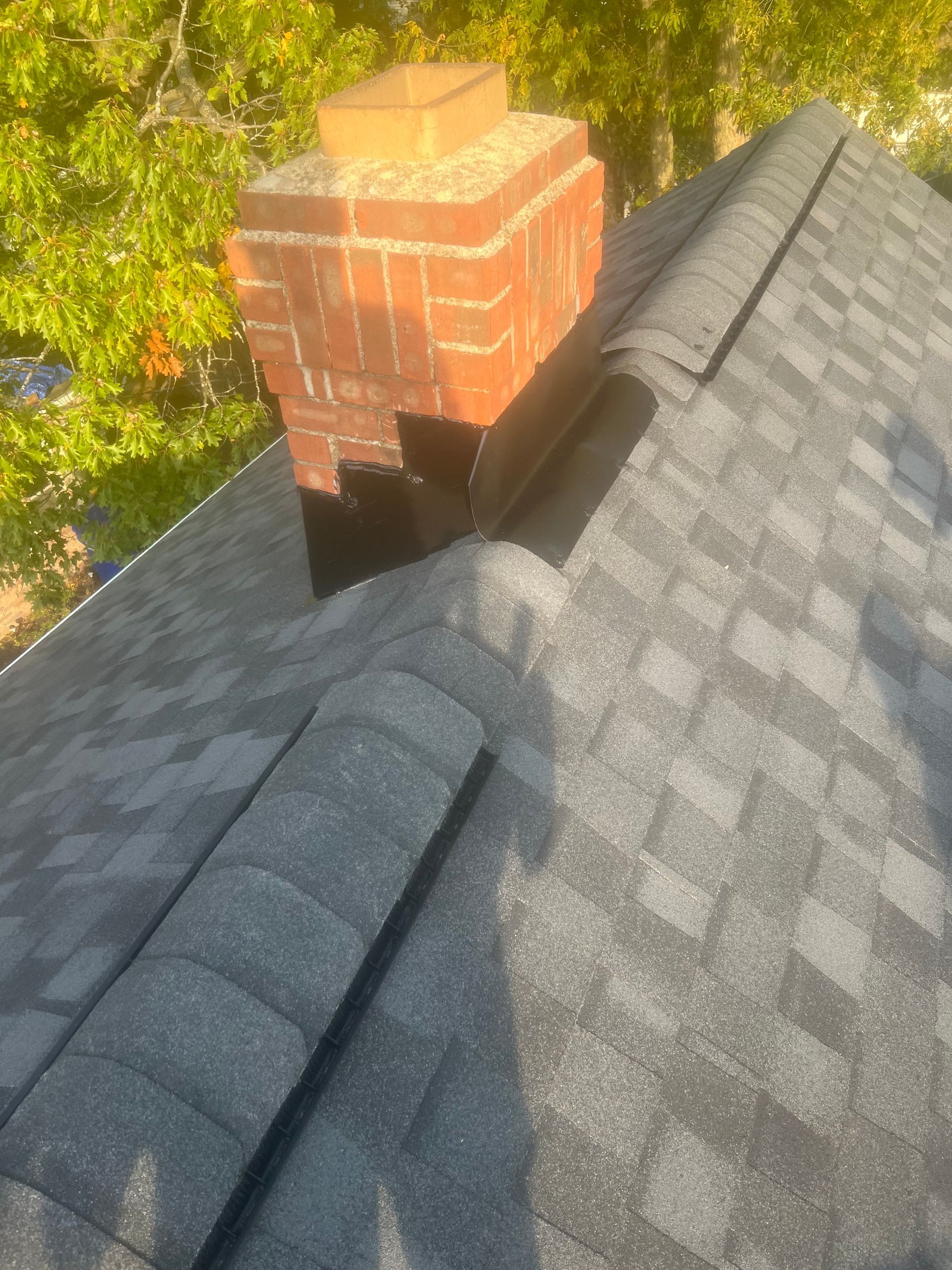 Brick chimney on a gray shingle roof, surrounded by flashing.