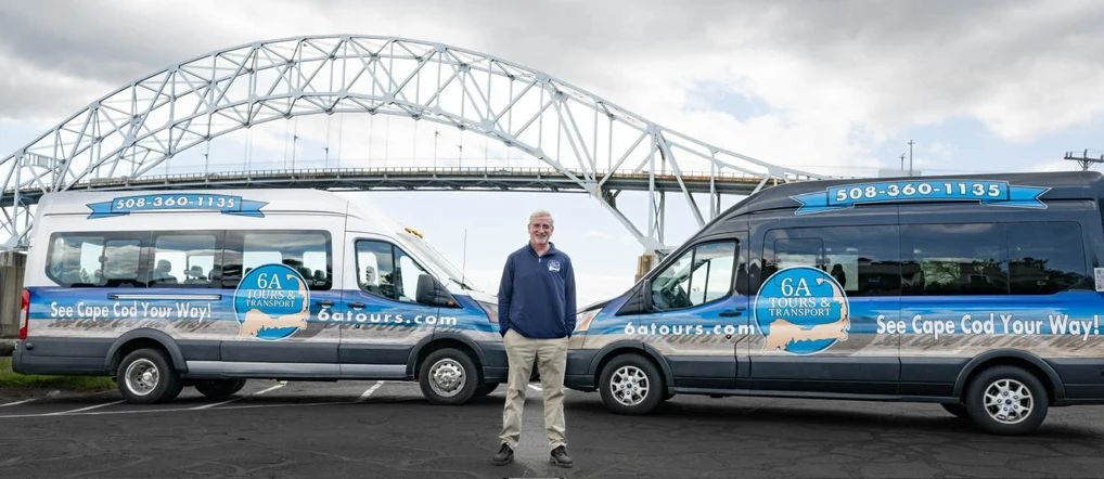 A person stands between two vans with Cape Cod tour branding in front of the Sagamore Bridge.