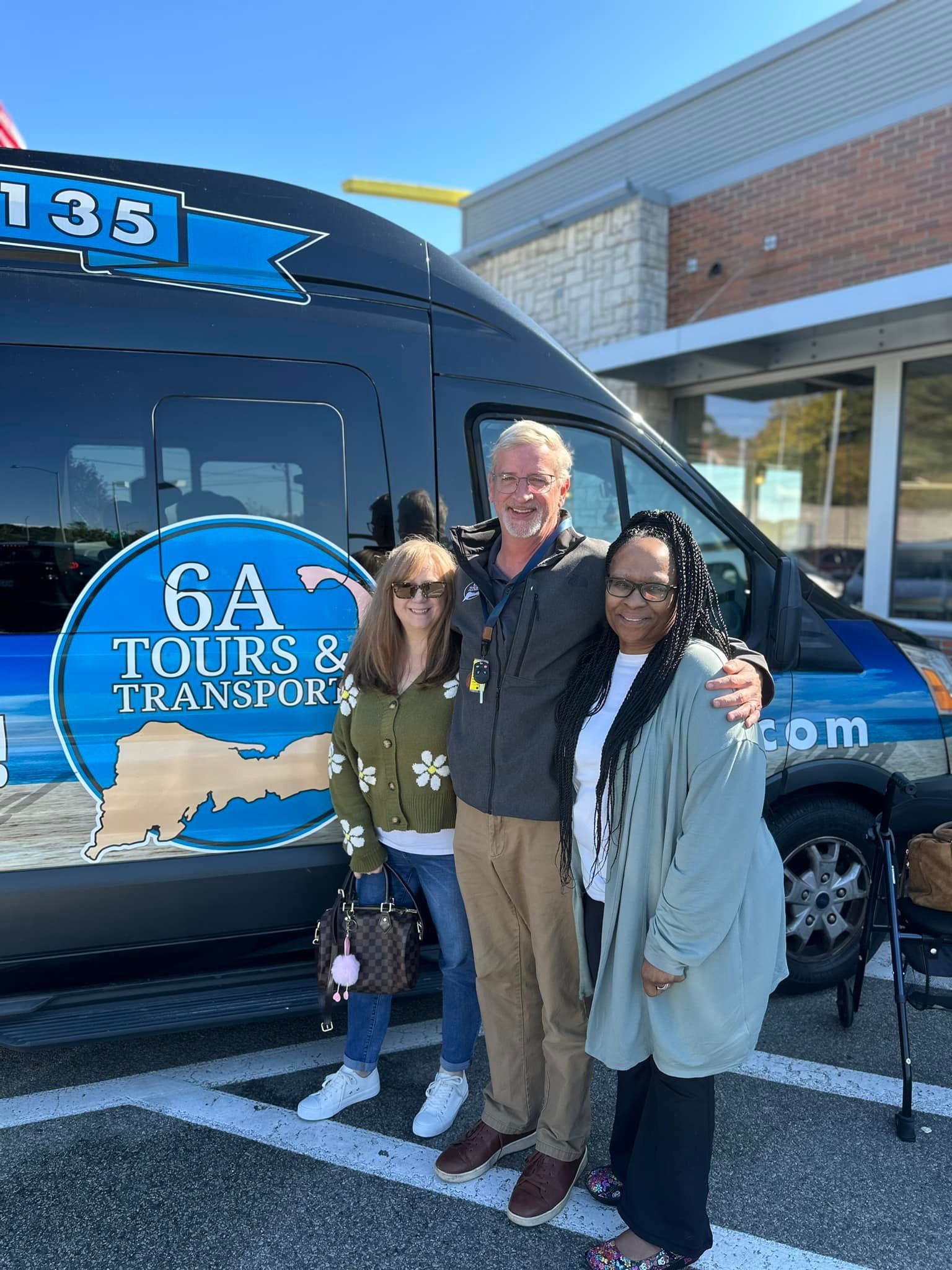 Three people stand smiling in front of a black van labeled
