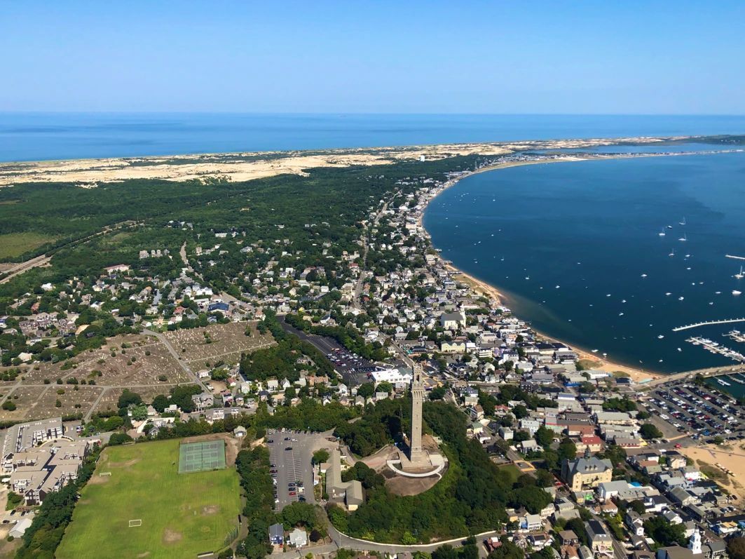 Aerial view of the Pilgrim Monument in Provincetown, Massachusetts, overlooking the town, harbor, and Cape Cod coastline.