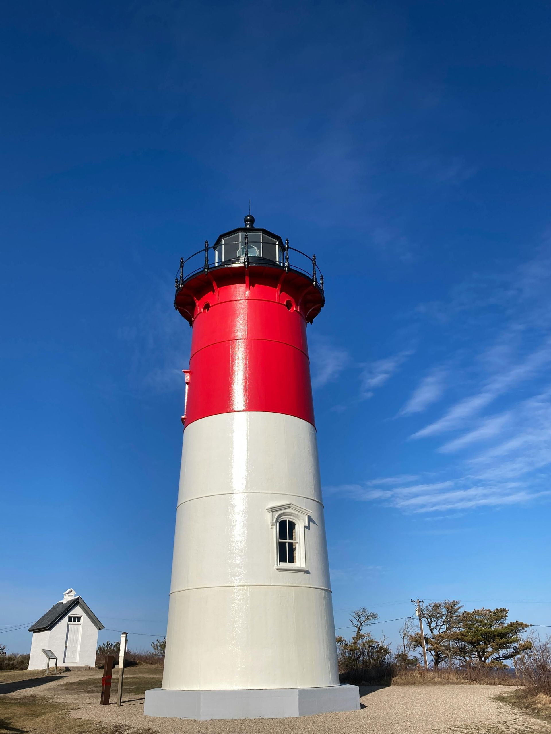 A red and white lighthouse stands against a clear blue sky, with a small white building visible in the background.