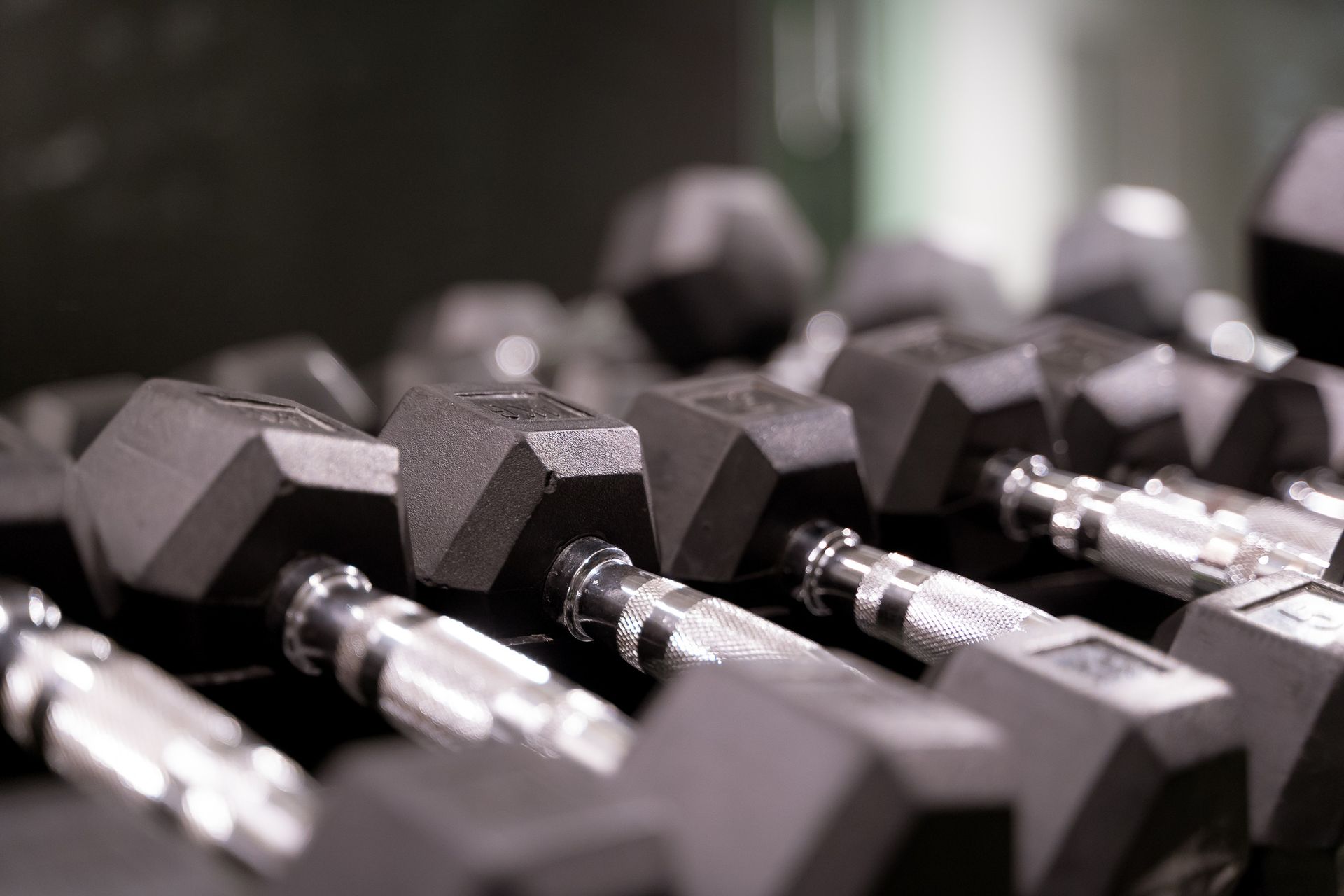 Zwarte zeshoekige dumbbells op een rij in een fitnessrek met een wazige achtergrond.