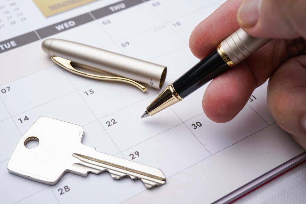 Hand Holding a Pen Over a Calendar Beside a Silver Key and Keychain — MoneySmith Group In Kingscliff, NSW
