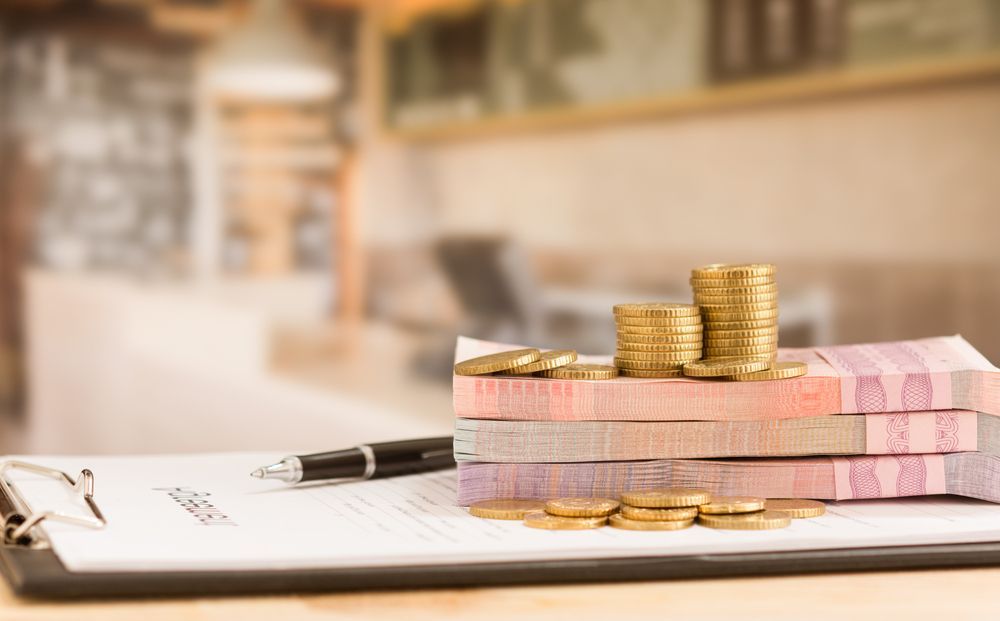 A Stack of Money and Coins on Top of a Clipboard With a Pen — MoneySmith Group In Kingscliff, NSW