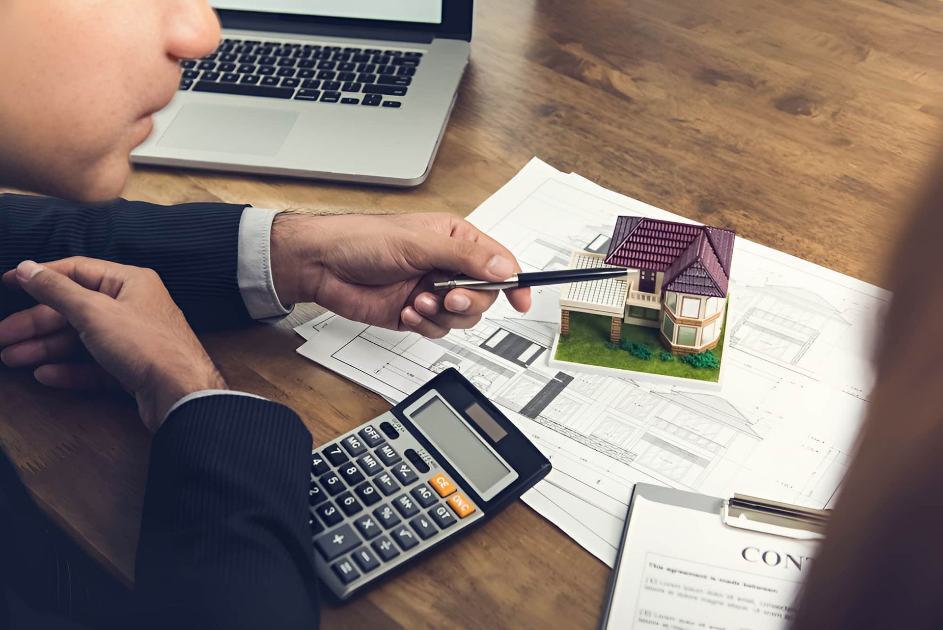 A Man is Sitting at a Table With a Calculator and a Model House — MoneySmith Group In Kingscliff, NSW