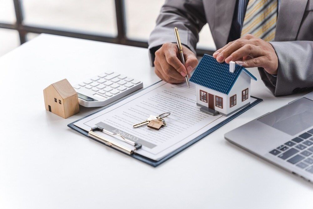 A Man is Sitting at a Desk With a Model House and Keys — MoneySmith Group In Northern Rivers, NSW
