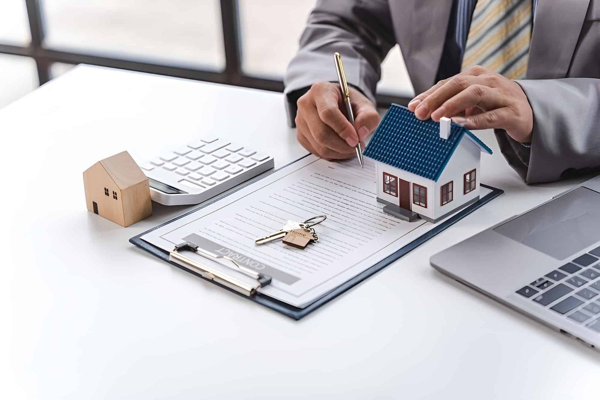 A Man is Sitting at a Desk With a Model House and Keys on a Clipboard — MoneySmith Group In Kingscliff, NSW