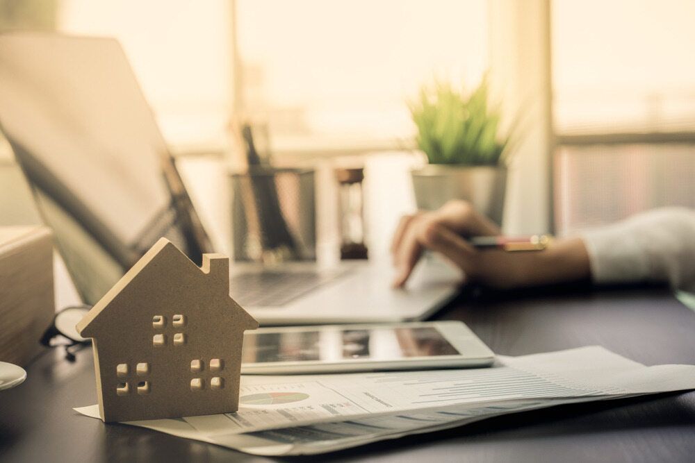 A Model House is Sitting on a Desk Next to a Person Using a Laptop — MoneySmith Group In Kingscliff, NSW