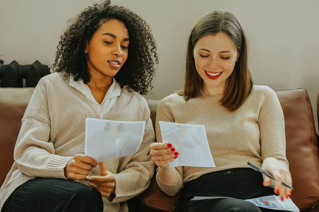 Two Women Are Sitting on a Couch Looking at Papers — MoneySmith Group In Kingscliff, NSW