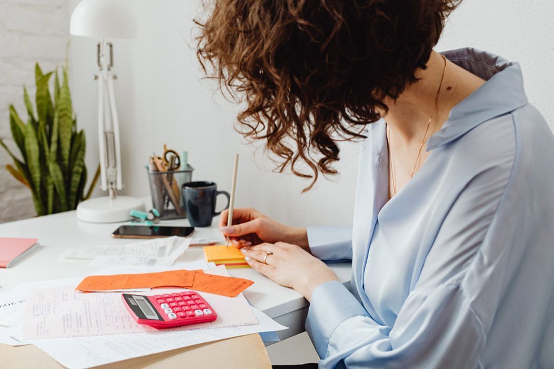 A Woman is Sitting at a Desk With a Calculator and a Pen — MoneySmith Group In Kingscliff, NSW