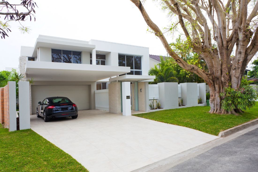 A modern white two-story house with a flat roof, a car in the garage, and a large tree in the front yard.