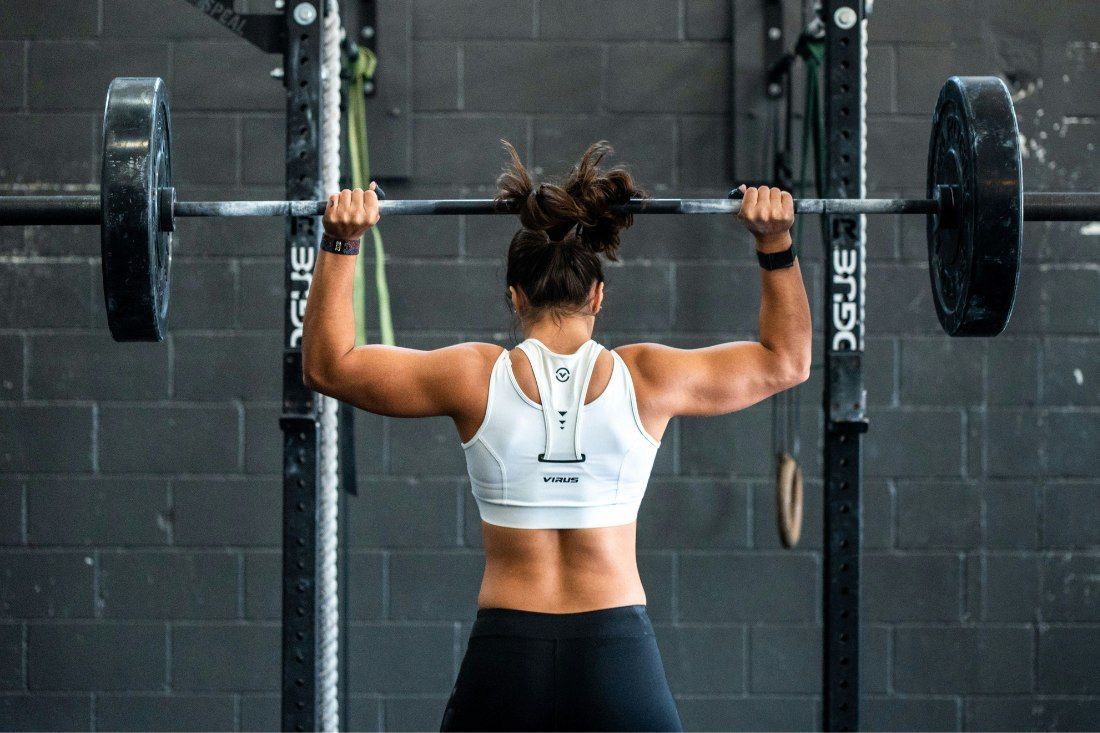 A Woman is Lifting a Barbell Over Her Head in a Gym — MoneySmith Group In Kingscliff, NSW