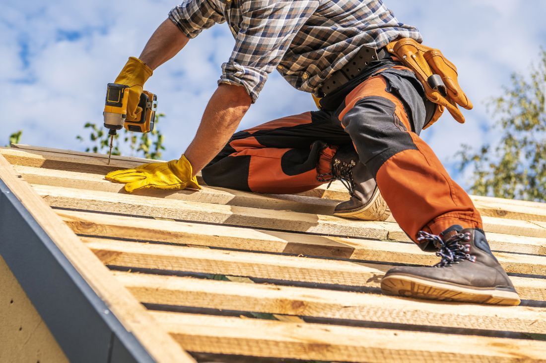 A Man is Working on a Wooden Roof With a Drill — MoneySmith Group In Kingscliff, NSW