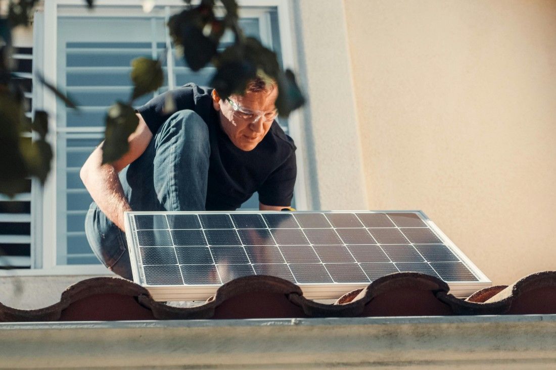 A person wearing safety glasses installs a solar panel on a tiled roof.