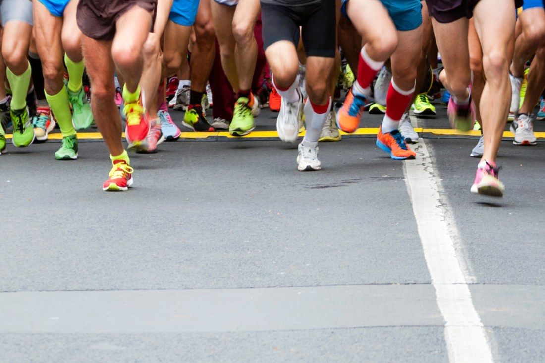 Low angle view of many runners' legs and feet in sneakers crossing a white starting line on asphalt.