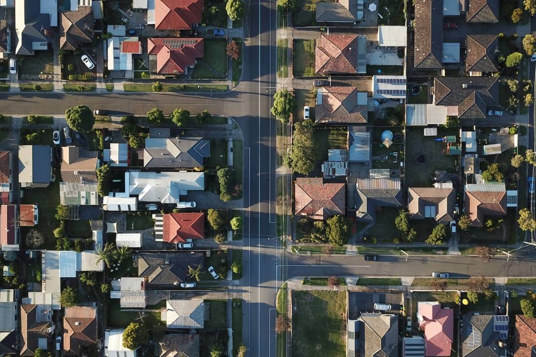 An aerial, top-down view of a suburban neighborhood featuring houses with various roof colors, tree-lined streets, and lots.
