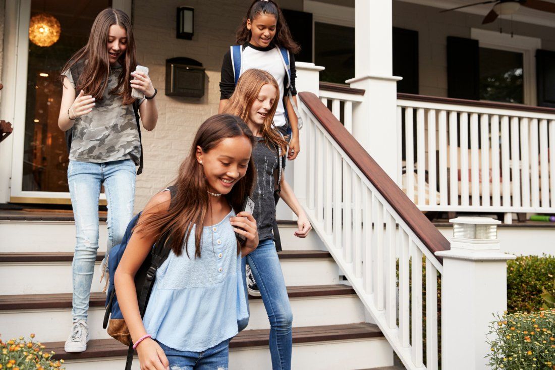 Four people walk down the front steps of a house carrying backpacks.