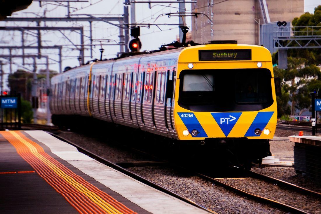 A yellow and blue Public Transport Victoria commuter train arriving at a railway station platform.