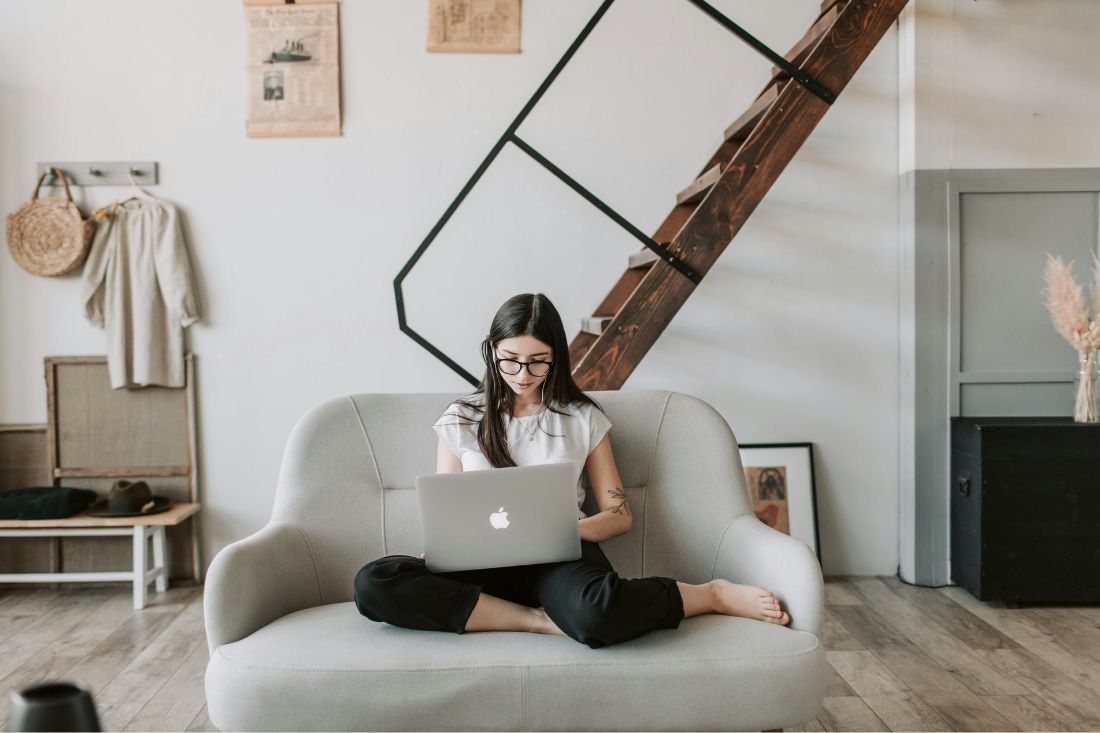 A woman sitting cross-legged on a light-colored armchair, using a laptop