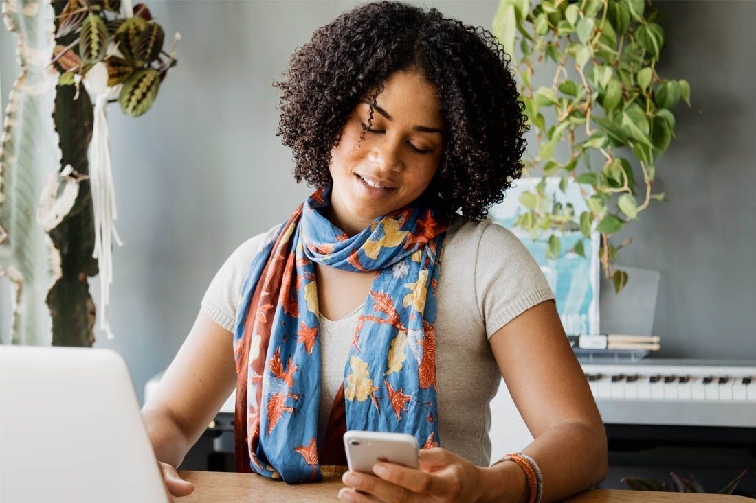 A Woman is Sitting at a Table Using a Laptop and a Cell Phone — MoneySmith Group In Kingscliff, NSW
