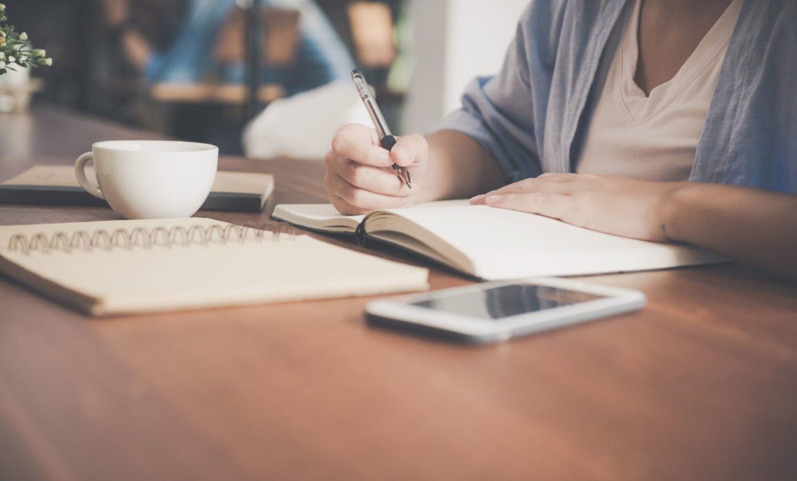 A Woman is Sitting at a Table Writing in a Notebook — MoneySmith Group In Coolangatta, QLD