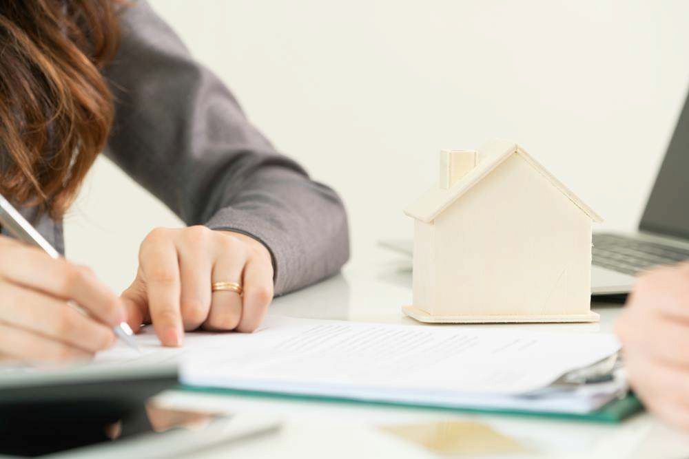 Person Writing at a Desk Beside a Small House Model and Laptop — MoneySmith Group In Kingscliff, NSW