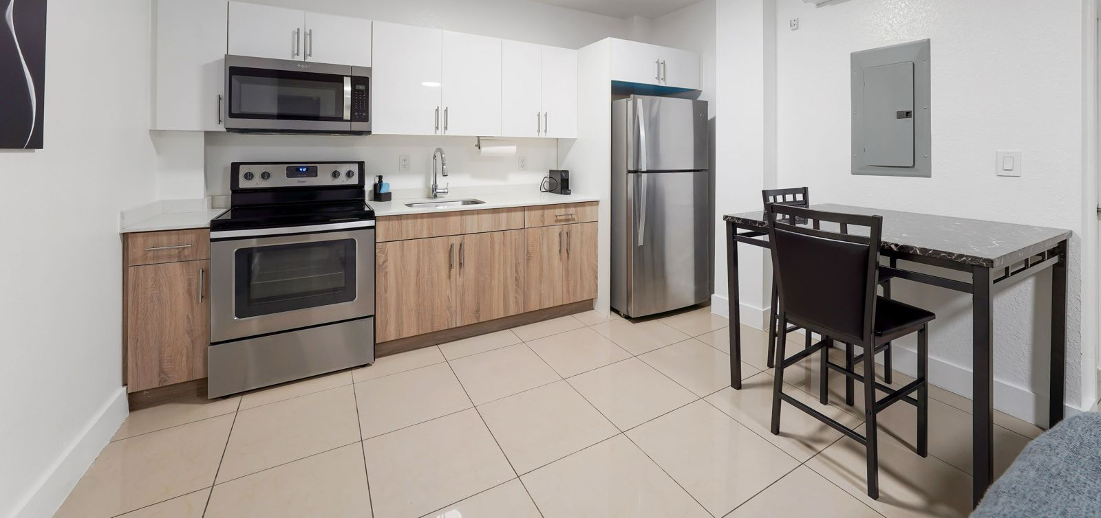 A modern kitchen with light wood lower cabinets, white upper cabinets, stainless steel appliances, and a small dining set.