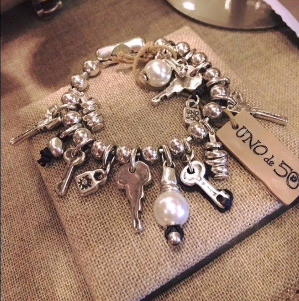 Braccialetto in argento con ciondoli, chiavi, perline e una perla, appoggiato su una superficie ricoperta di tela di iuta.