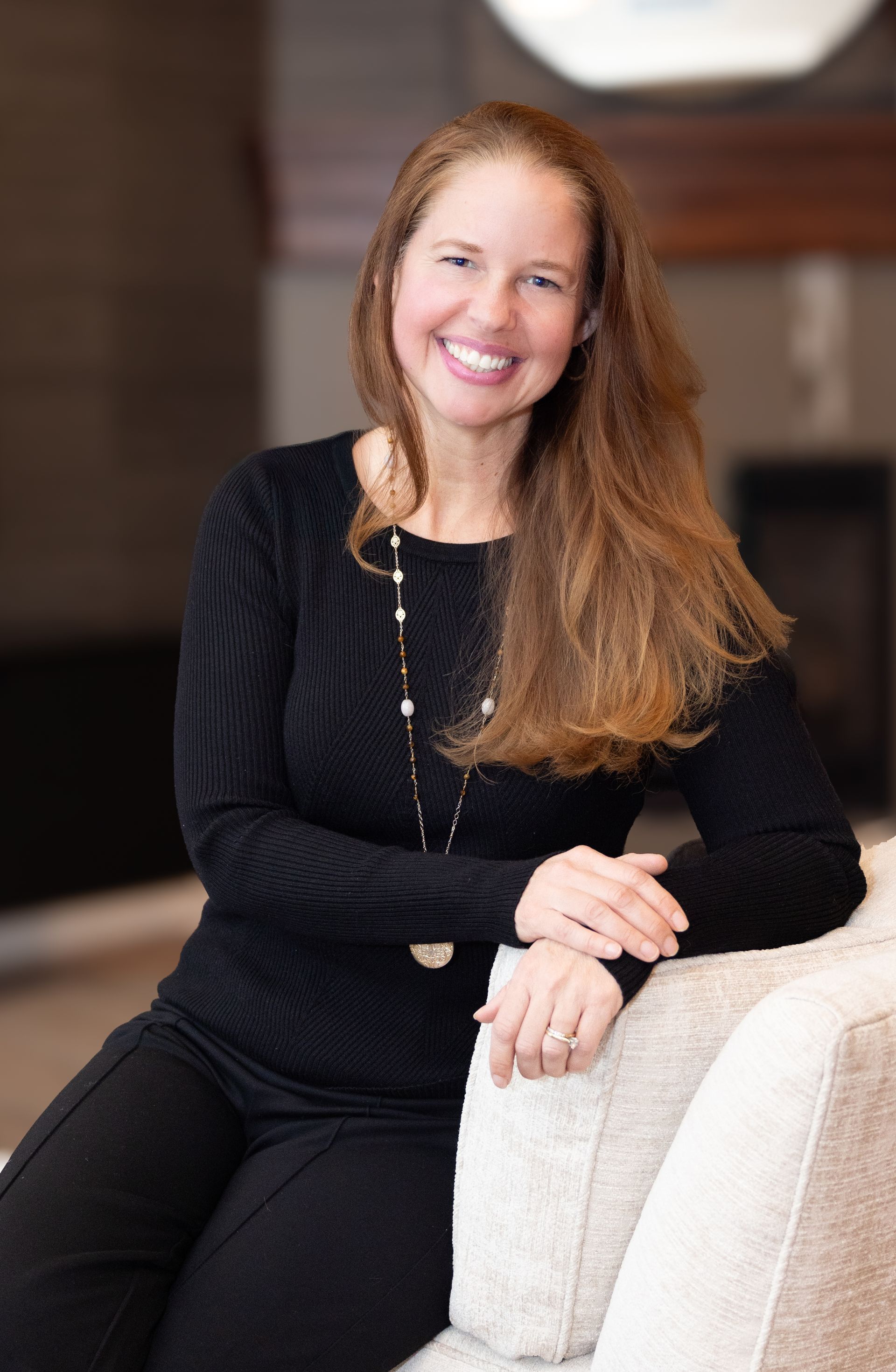 A woman in a black sweater is sitting on a couch and smiling