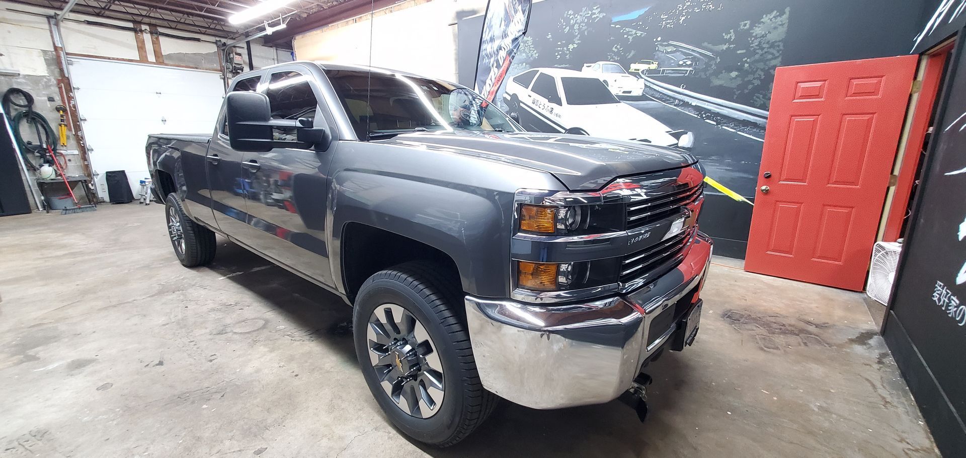 Black pickup truck in a garage, front-left view, with chrome bumper and red door in background