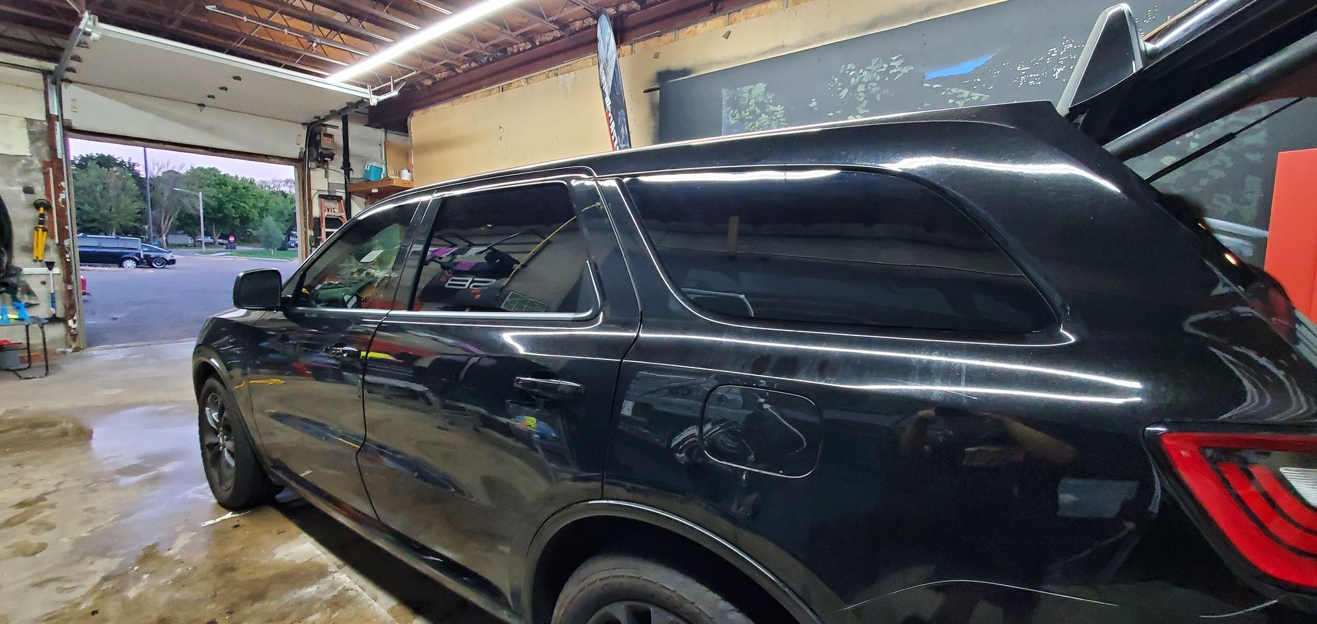 Black SUV parked inside a garage bay, side view with open rear hatch and red taillight visible