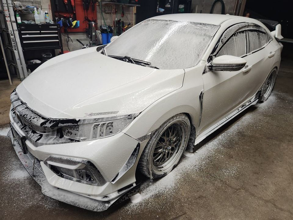 White sports sedan covered in snow or foam in a garage, front-left view