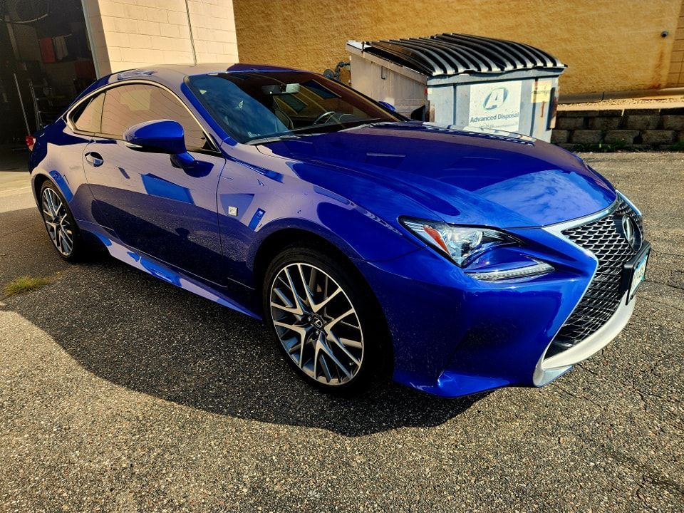 Blue Lexus coupe parked beside dumpsters in a lot at night