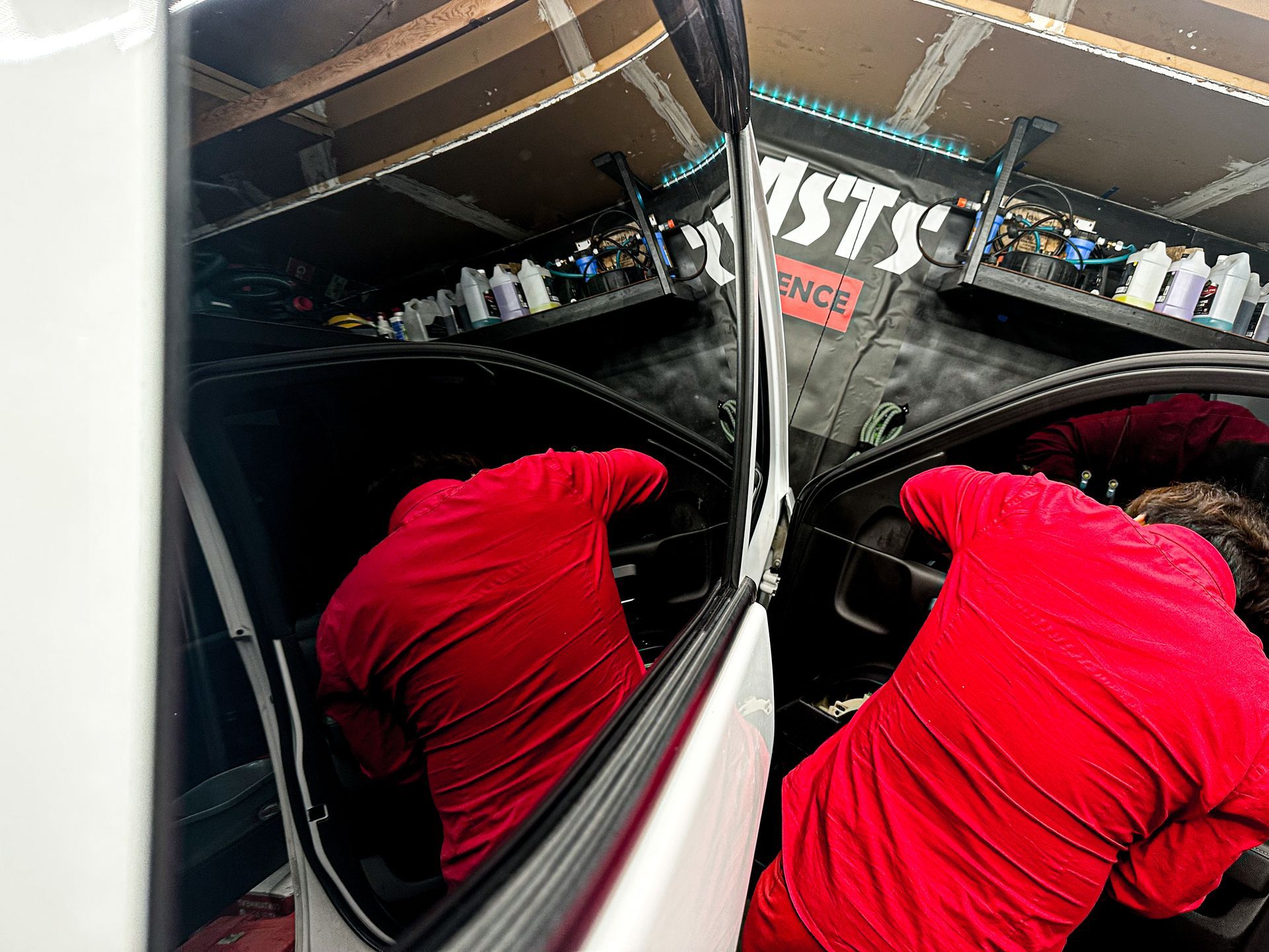 A man in a red shirt is working on a car window.