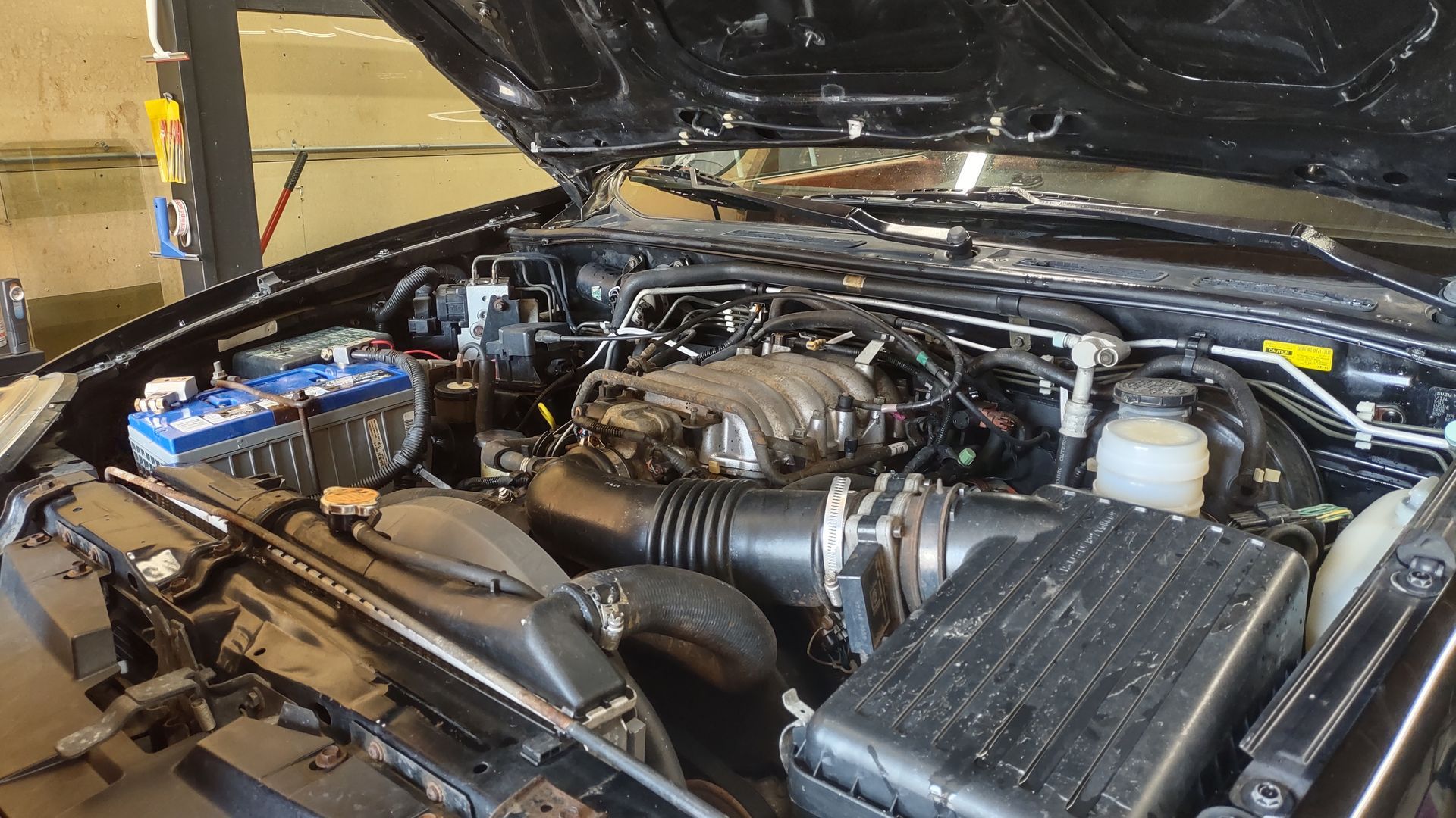Open car hood showing an engine bay with black and blue components in a garage.
