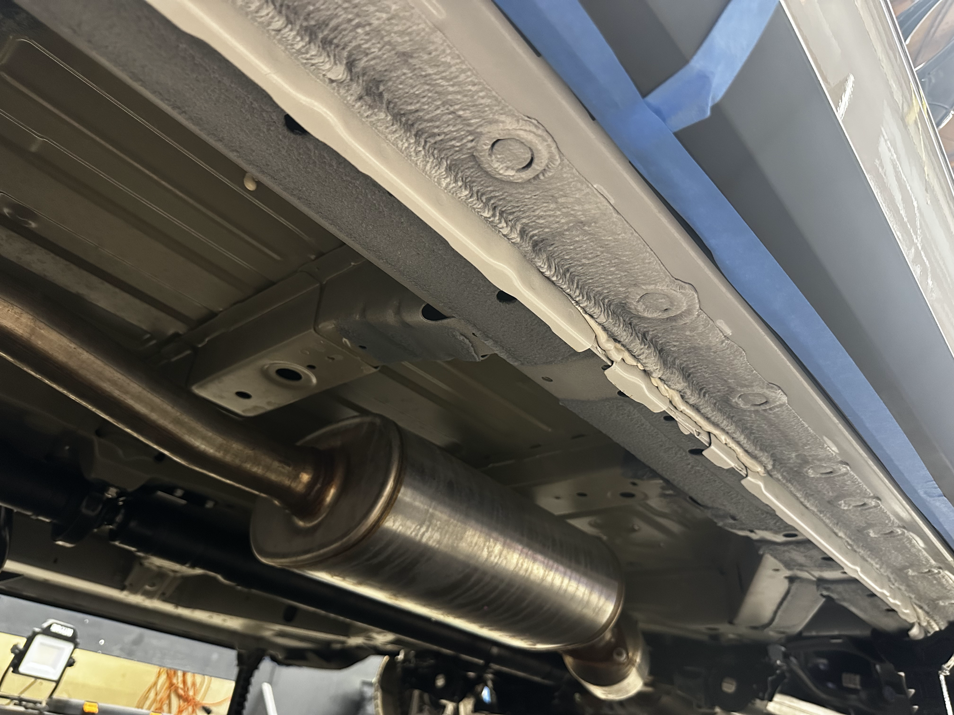 Undercarriage of a car showing a silver exhaust muffler and metal frame panels