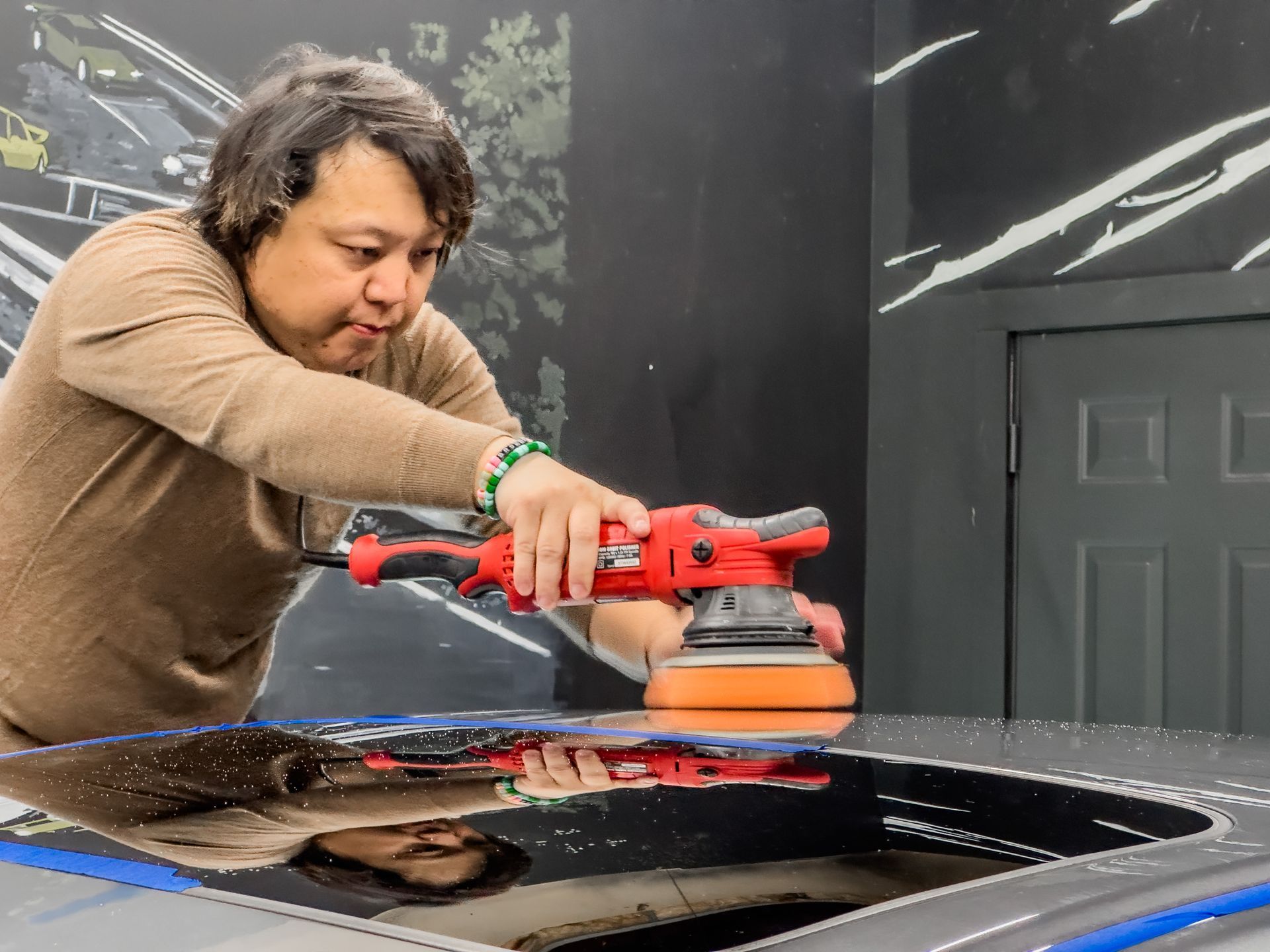 a man is polishing the roof of a car with a machine .