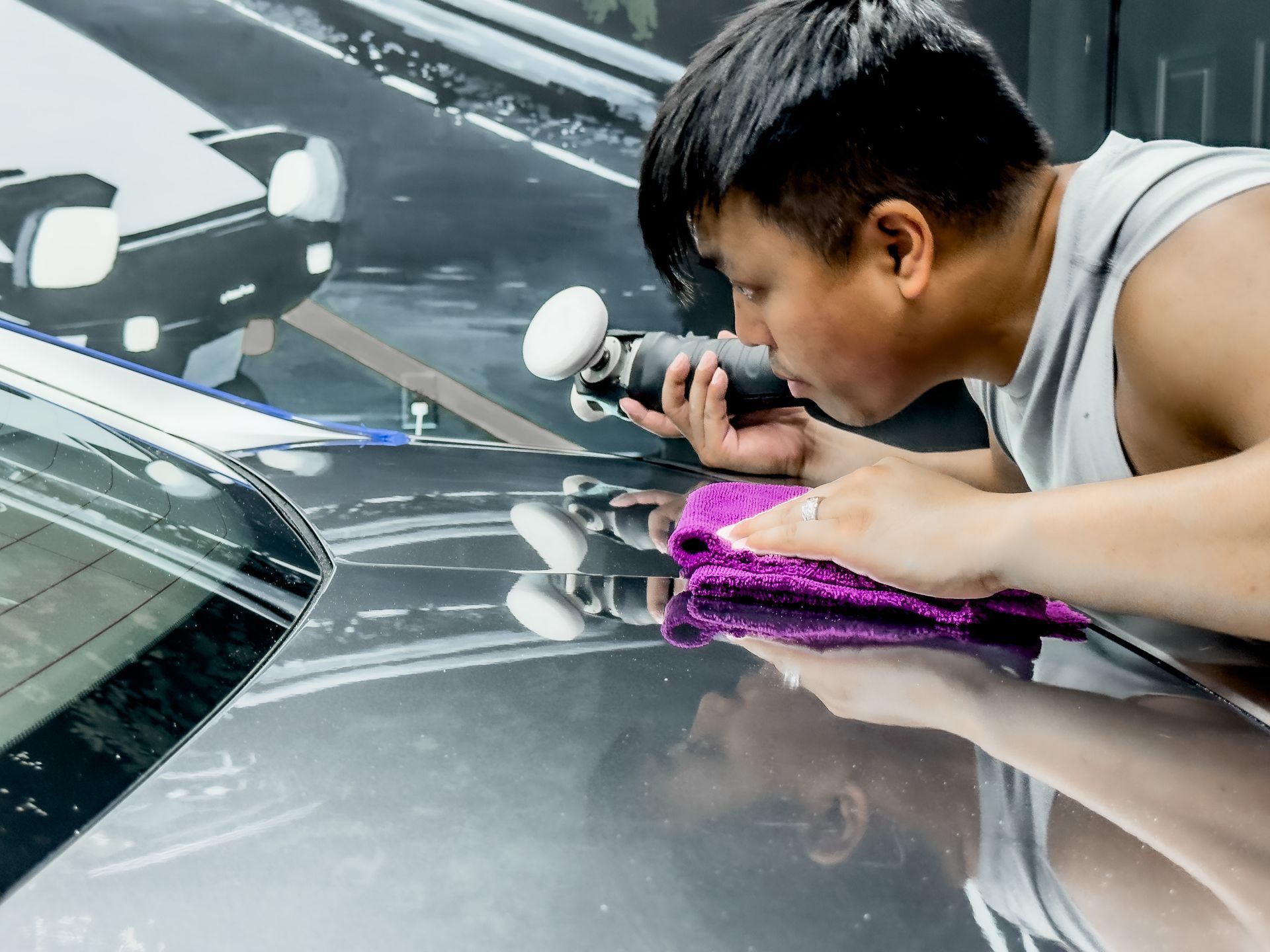 a man is polishing the hood of a car with a polisher .