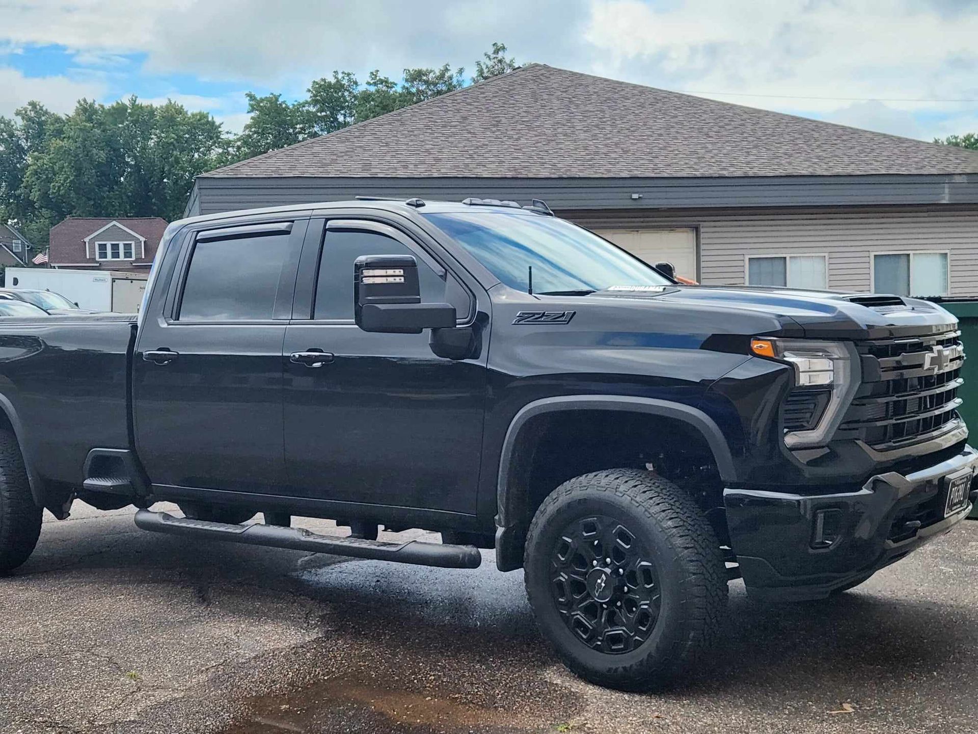 Black lifted pickup truck parked in a driveway beside a house