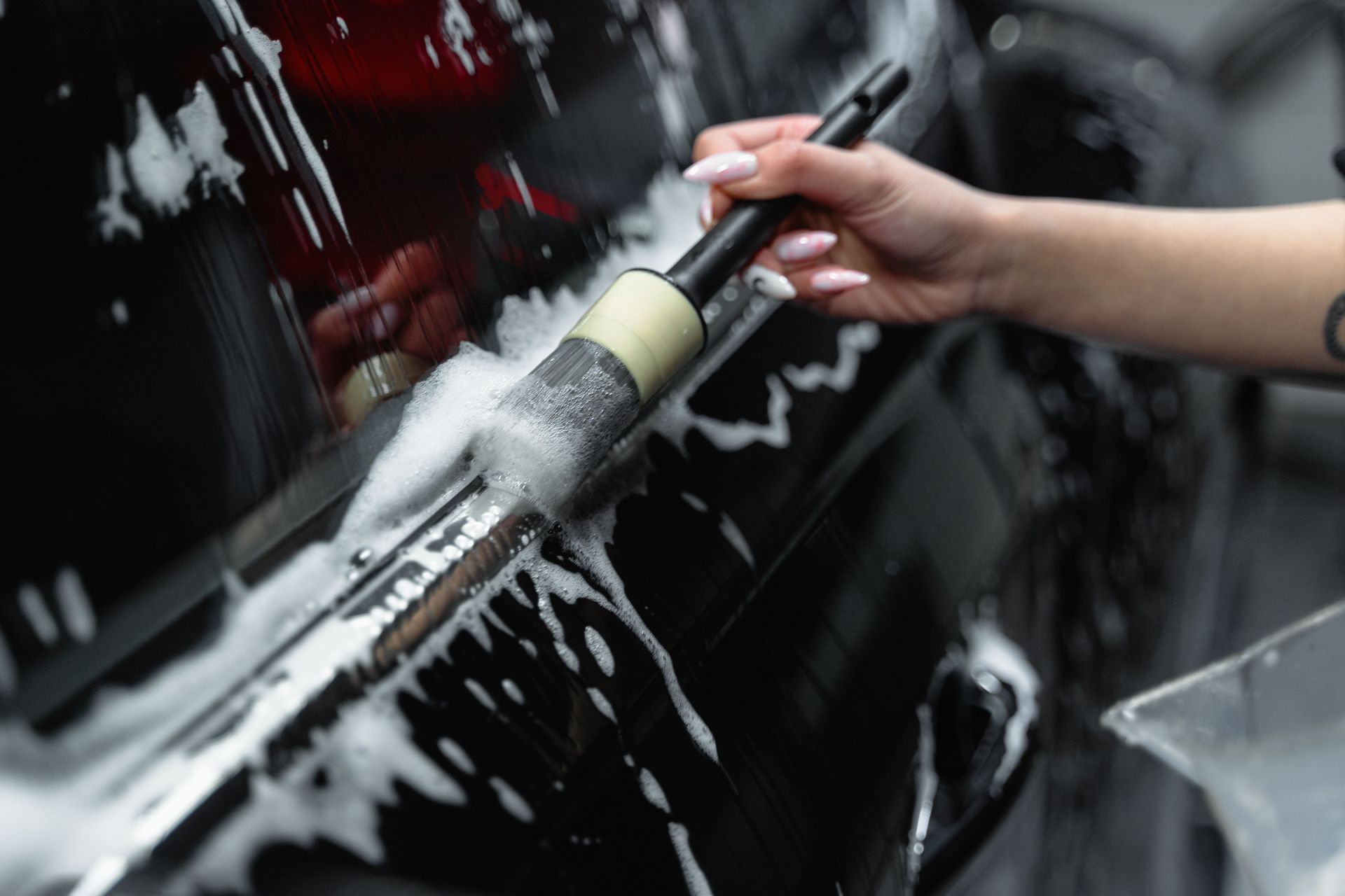Hand holding a squeegee cleaning soap-covered black car windshield