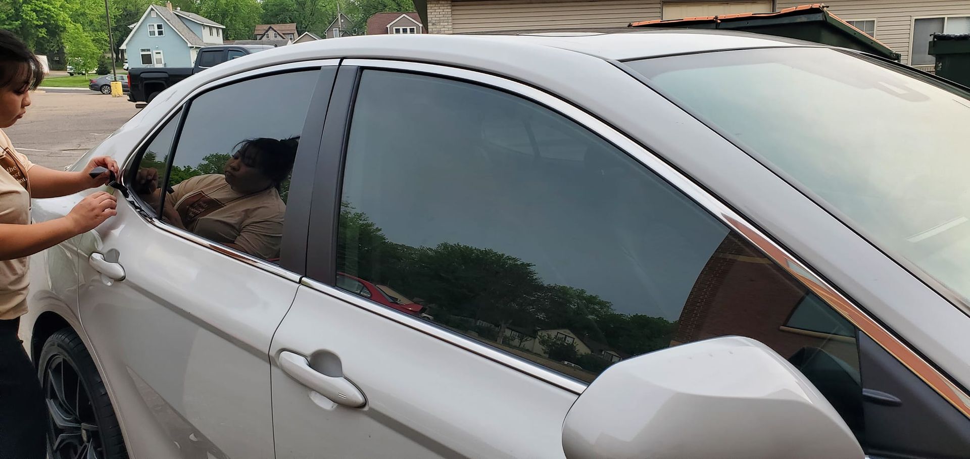 Person washing the side window of a silver sedan outdoors in a driveway